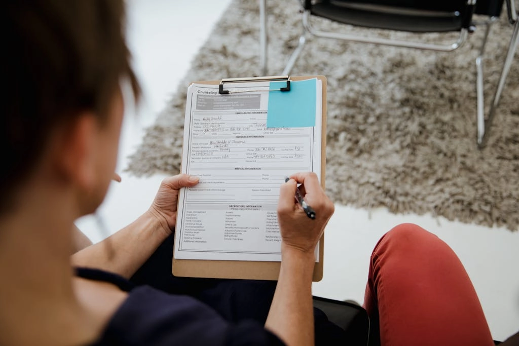 An adult woman writing on a counseling form during a business appointment in an office setting.